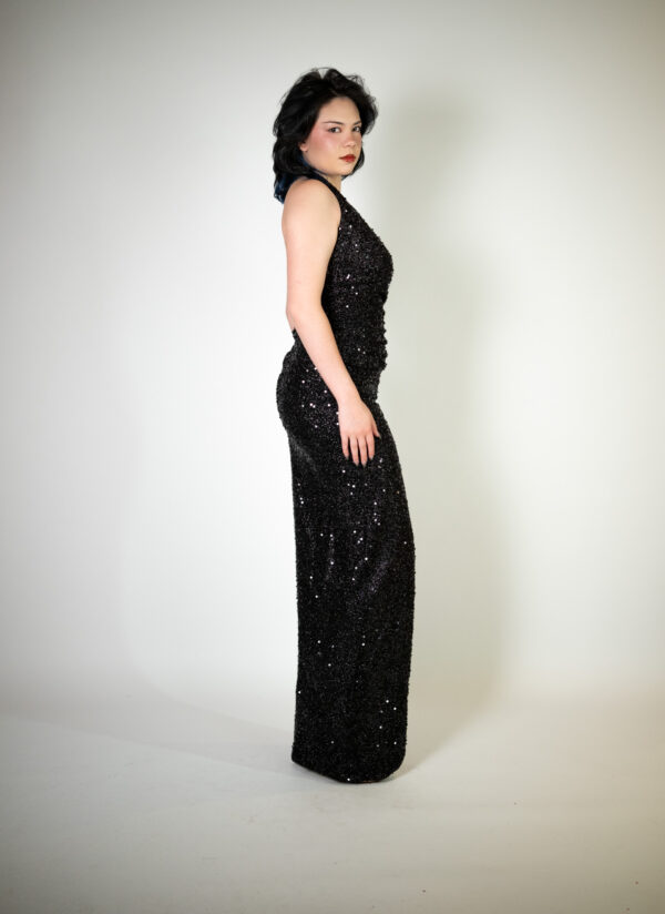 Alt text: "Black deep V-neck halter dress called Artisa, featuring a high slit and covered in sequins, perfect for special occasions."