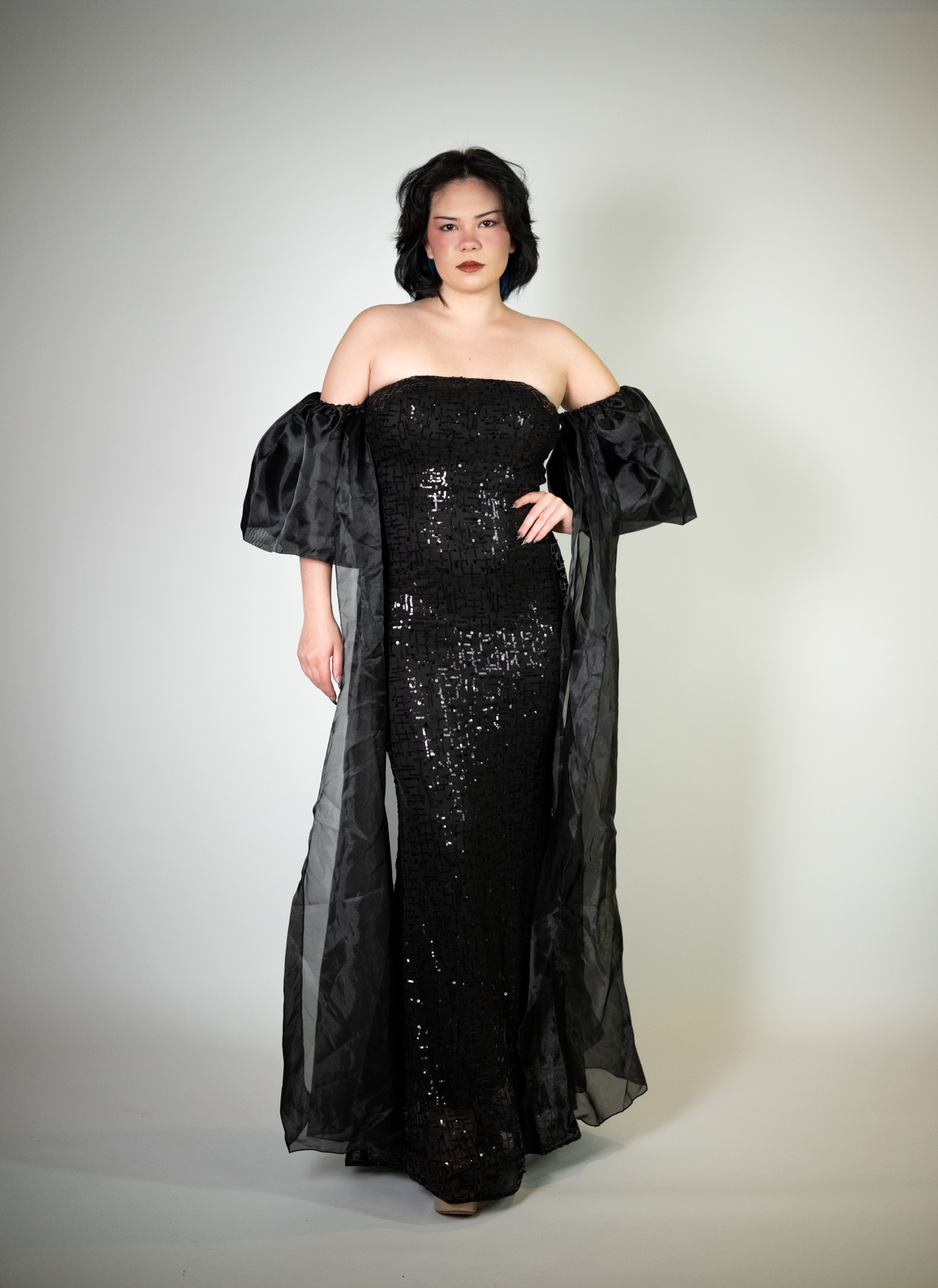 Alt text: "Sequin black strapless gown called Diva, featuring two chiffon sleeves, perfect for special occasions."