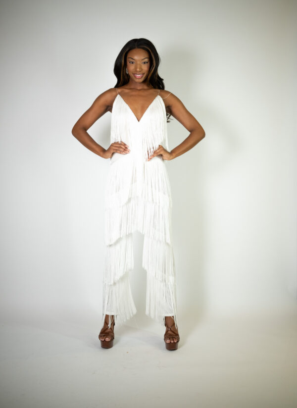 Alt text: "White V-neck jumpsuit called Giddy Up, featuring fringe tassels from top to bottom and straight legs, perfect for special occasions."