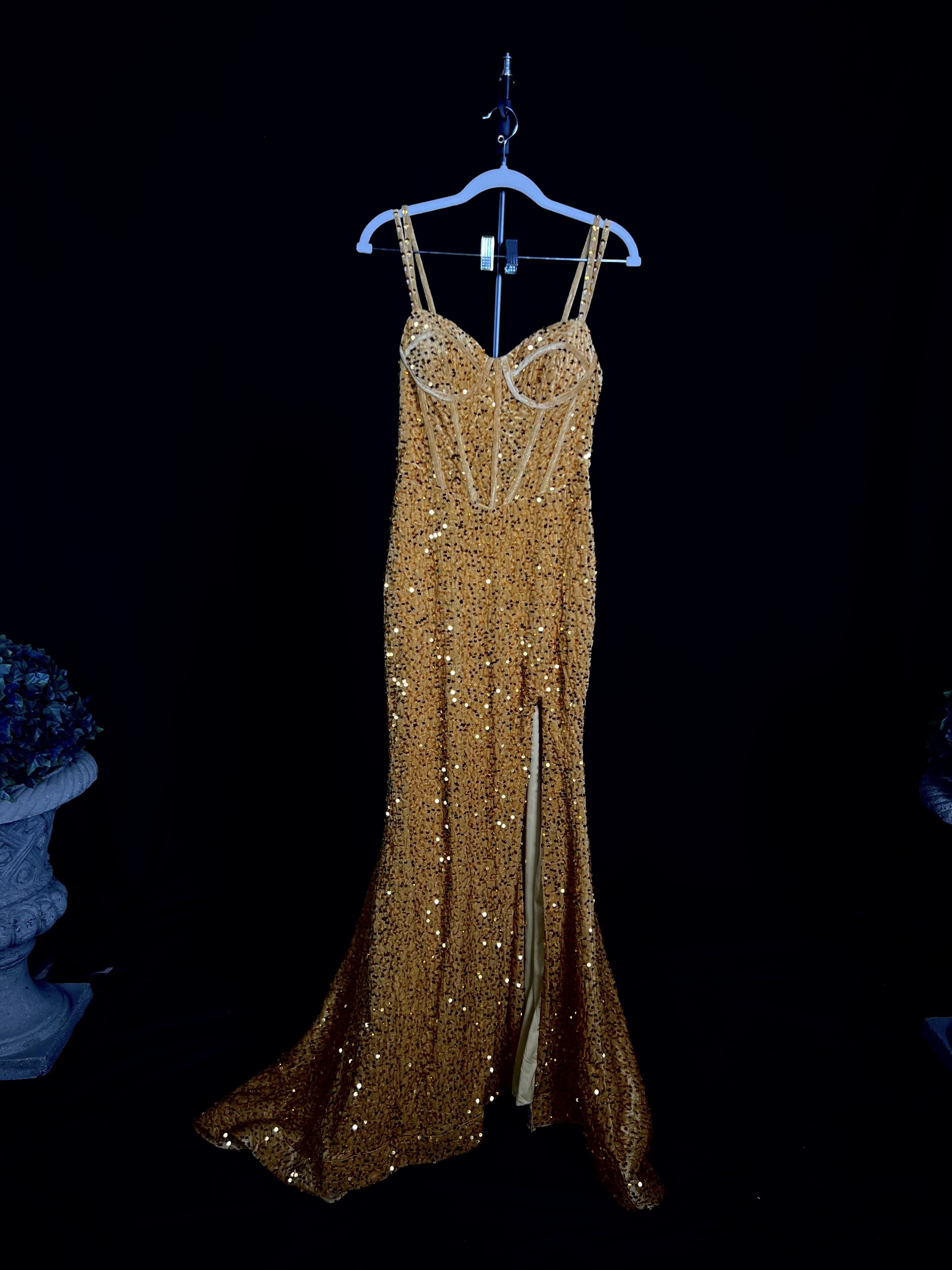 Introducing the Marigold Gown, a luxurious gold velvet evening gown perfect for your next gala or formal event. This exquisite dress features a built-in bustier and a corset back that enhance the silhouette, providing a flattering and sophisticated fit. Adorned with sequins, the gown sparkles elegantly, capturing attention with every turn. The long chapel-length train with a chunky hem adds a dramatic flair, making this gown a true statement piece. Ideal for glamorous evenings, the Marigold Gown ensures you stand out with unmatched elegance and style. Shine with grace and allure in this stunning gold velvet gown. --- Alt text: "Gold velvet evening gown called Marigold, featuring sequins, built-in bustier, corset back, and a long chapel-length train with chunky hem, perfect for formal occasions."