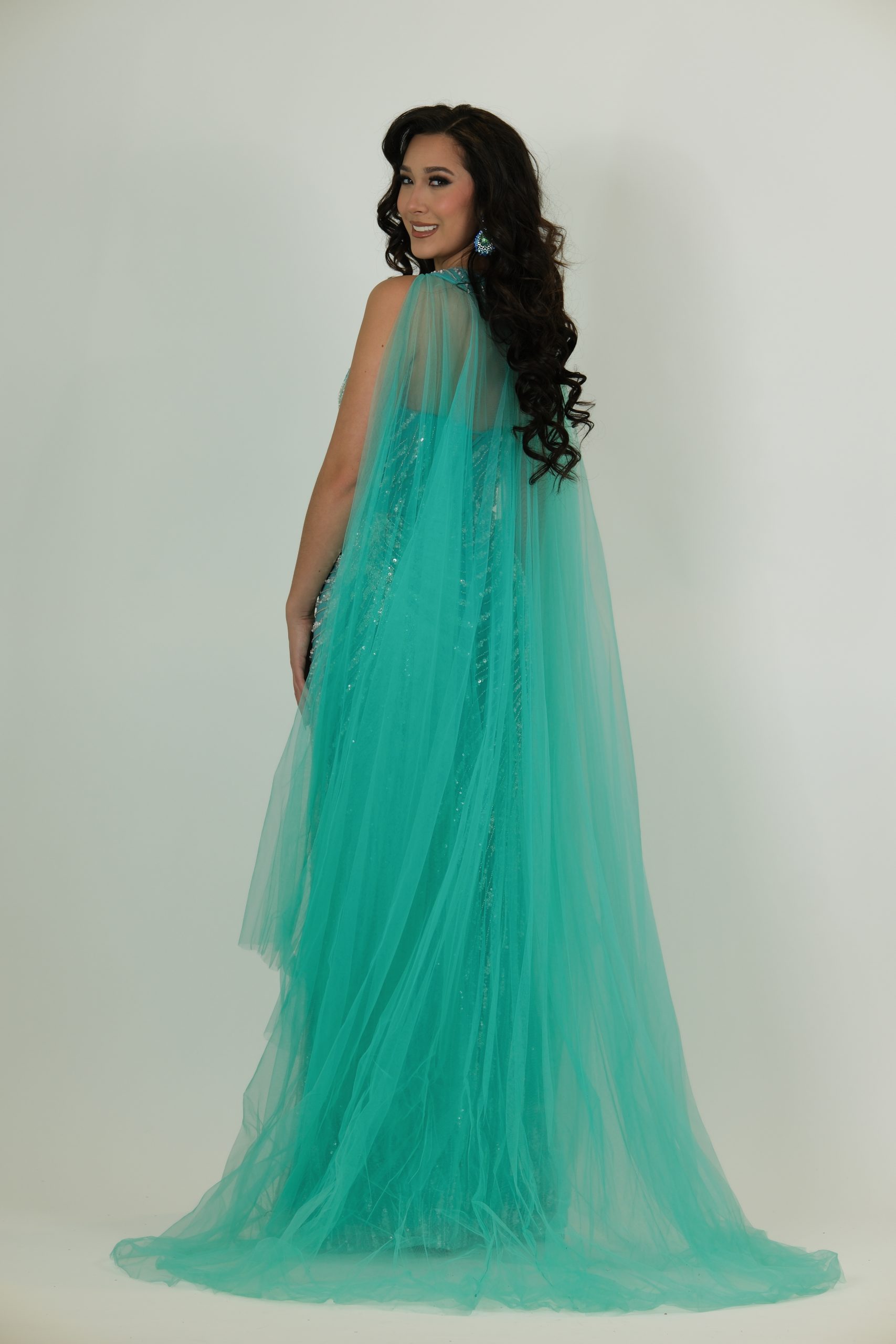 "Turquoise sequin gown called Aqua, featuring a V-neck bodice, silver sequin pattern, and a dramatic flowing tulle cape."