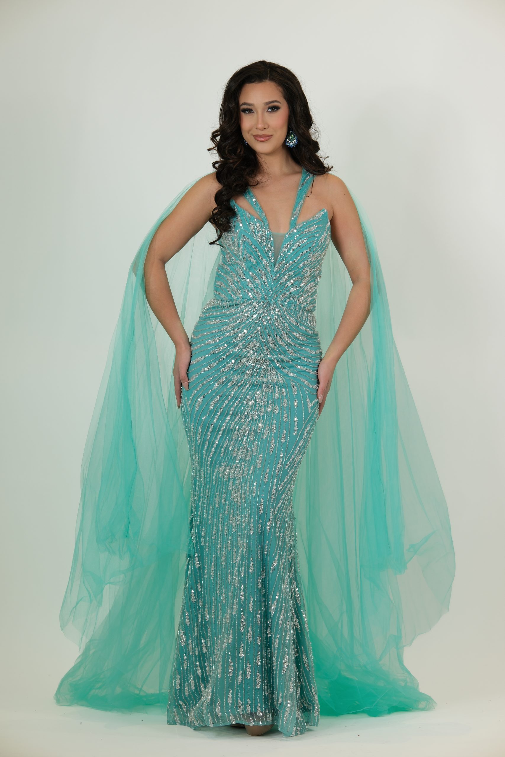 "Turquoise sequin gown called Aqua, featuring a V-neck bodice, silver sequin pattern, and a dramatic flowing tulle cape."