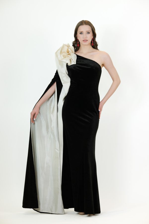 “Black one-shoulder velvet gown with ivory satin rosette and dramatic cascading cape.”