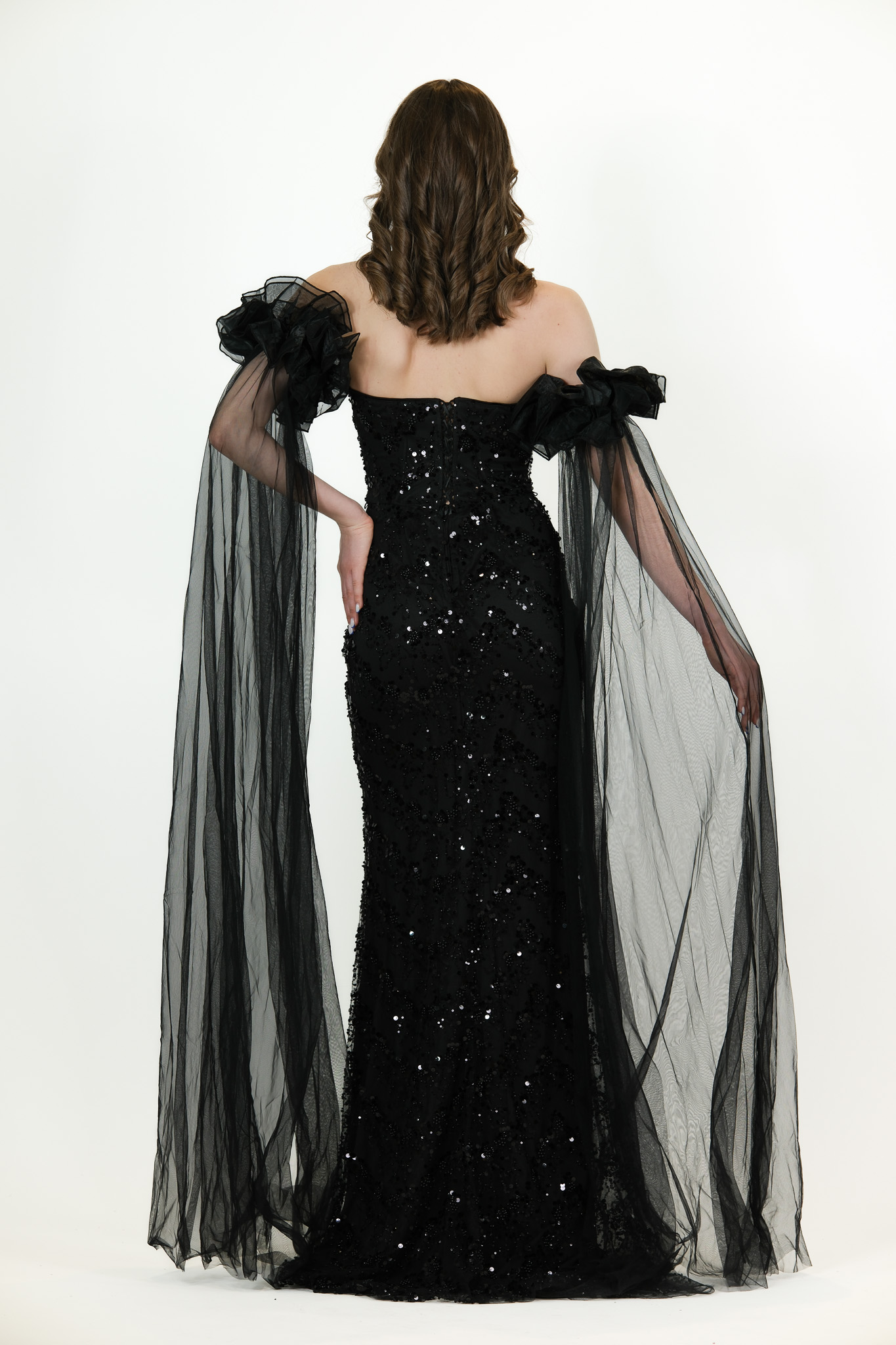 “Black sequin gown with sweetheart neckline and long draped off-shoulder tulle sleeves.”