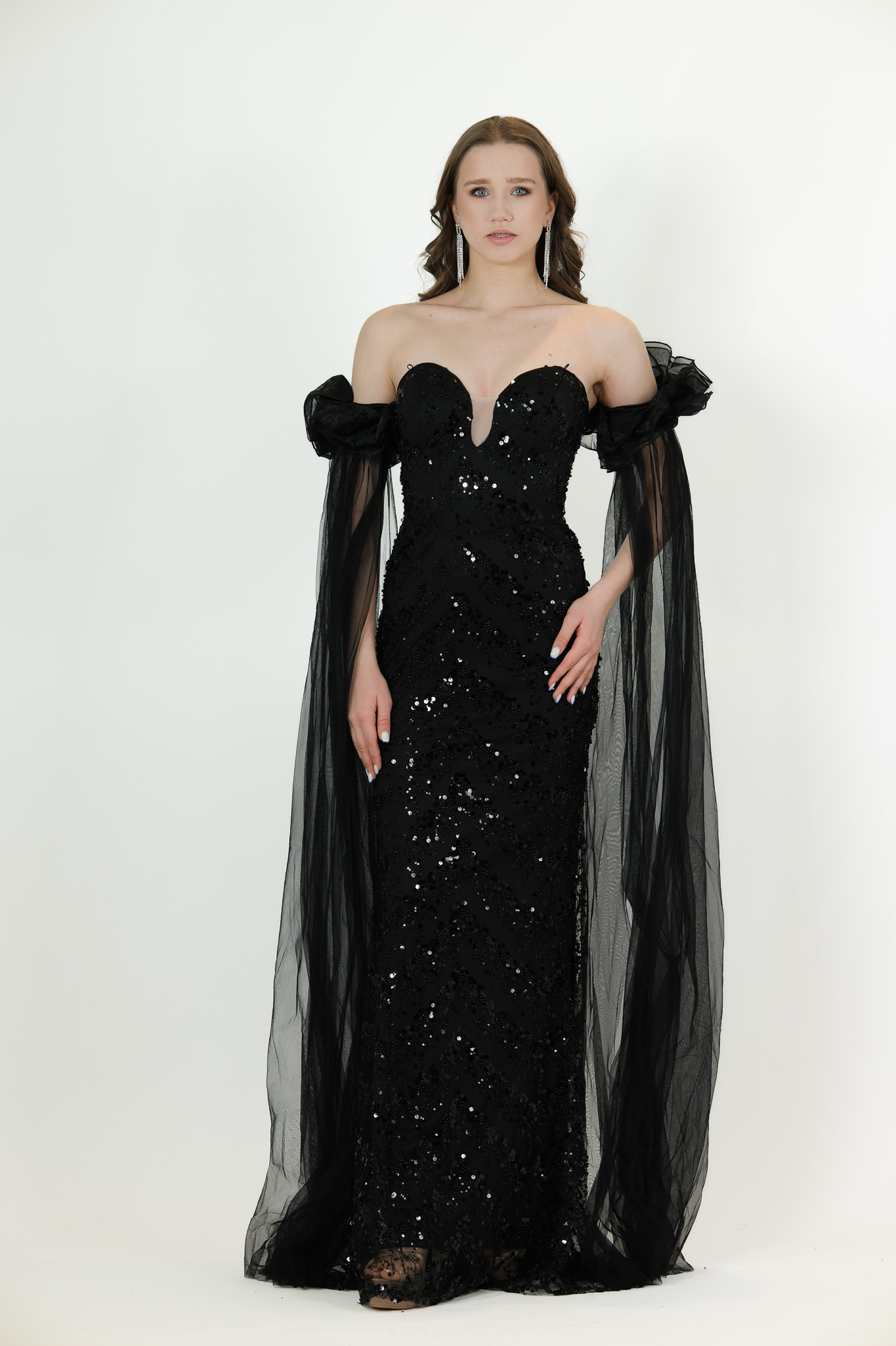 “Black sequin gown with sweetheart neckline and long draped off-shoulder tulle sleeves.”
