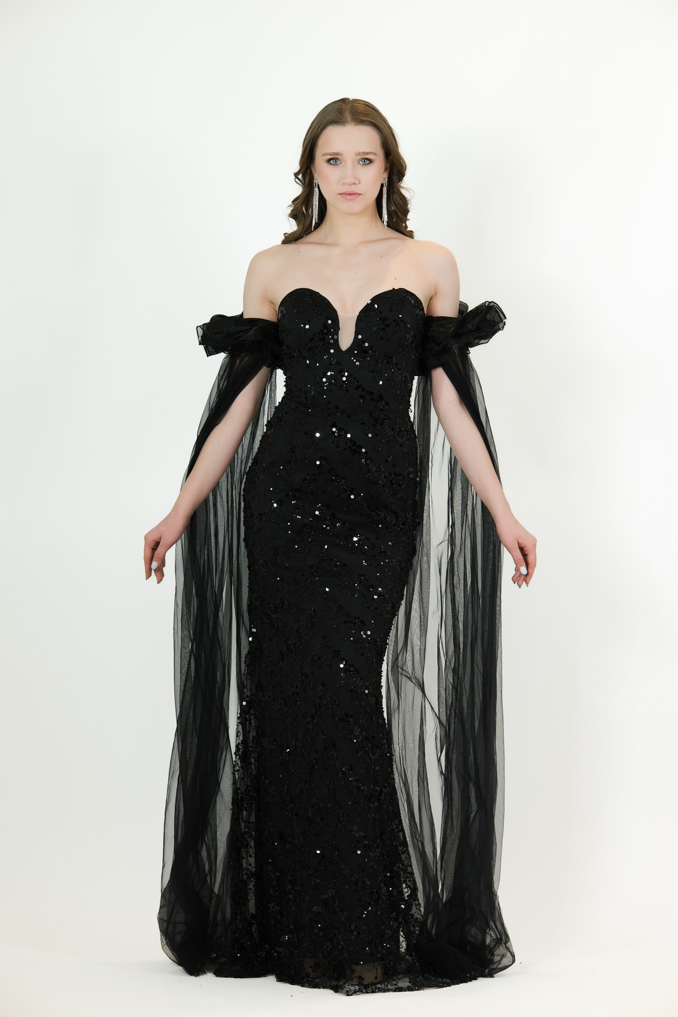 “Black sequin gown with sweetheart neckline and long draped off-shoulder tulle sleeves.”