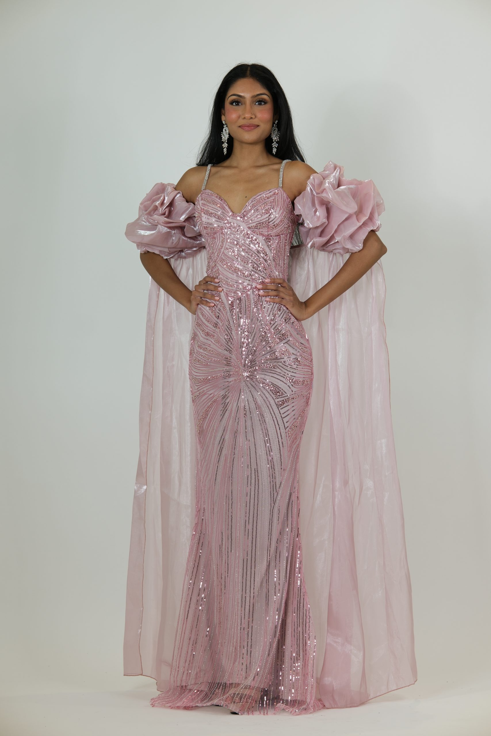 “Blush pink sequin gown with diamond straps, dramatic puff sleeves, and a long glossy cape.”