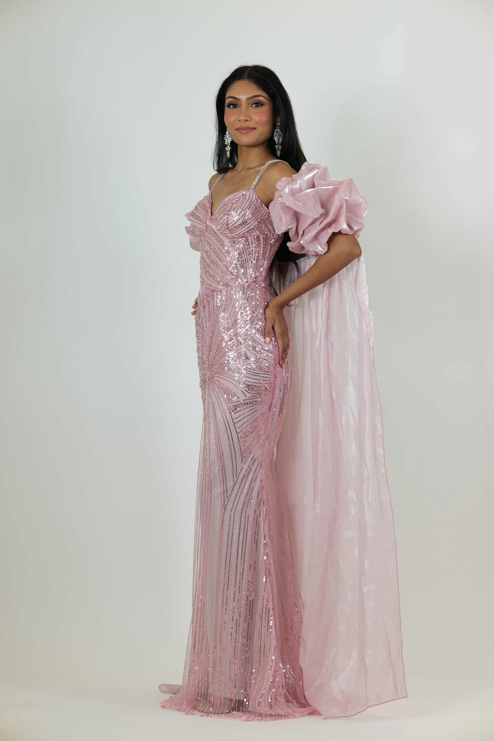 “Blush pink sequin gown with diamond straps, dramatic puff sleeves, and a long glossy cape.”