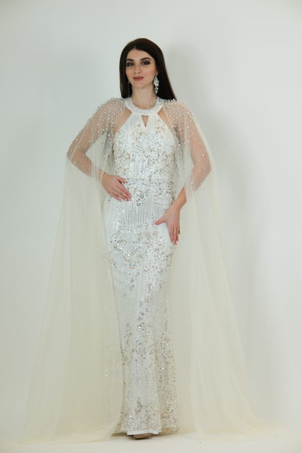 White and silver sequin gown called Marcella, featuring a pearl-studded sheer cape and a keyhole neckline, perfect for special occasions.