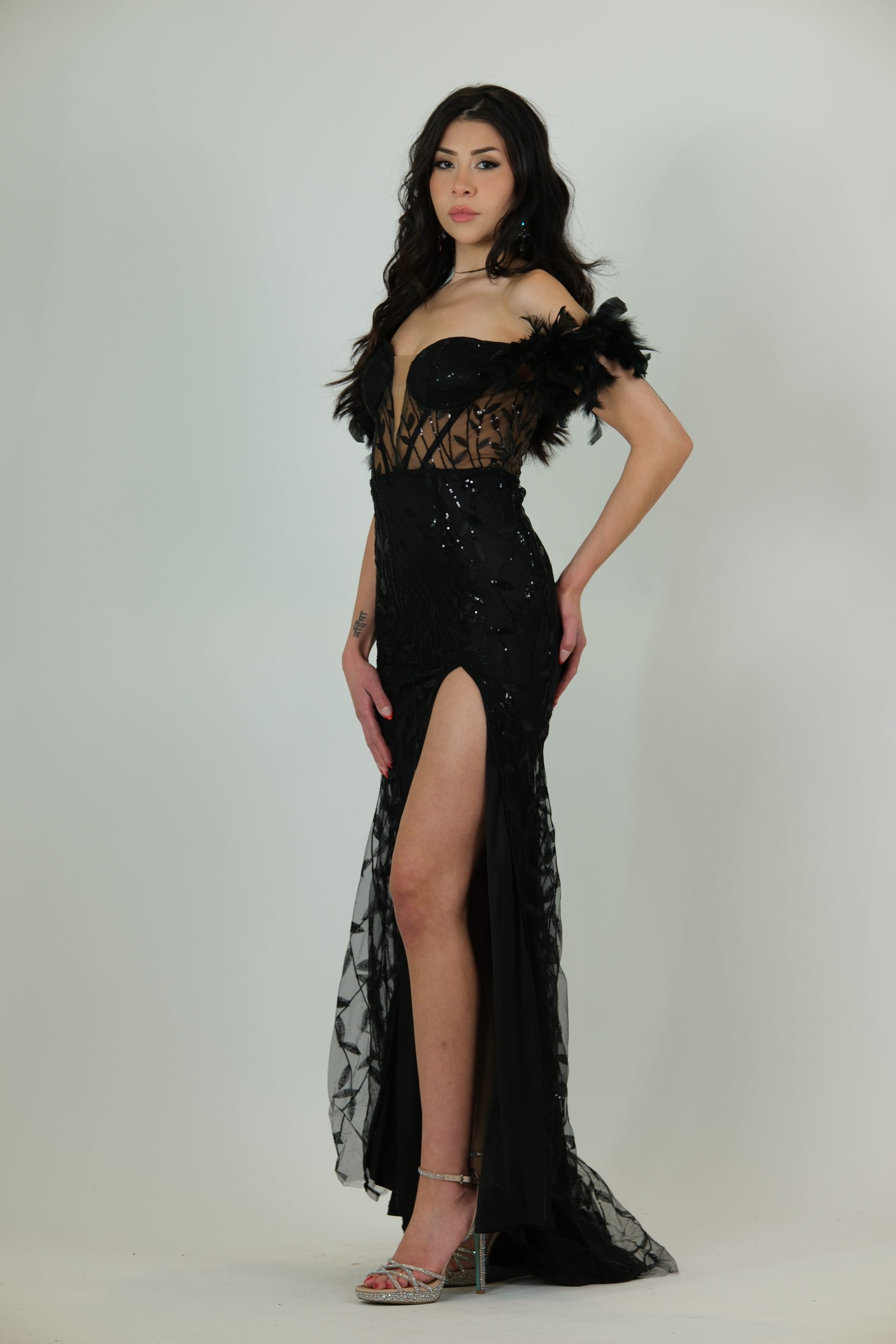 "Black sheer corset gown with feathered off-shoulder sleeves, sequin detailing, and a thigh-high slit."