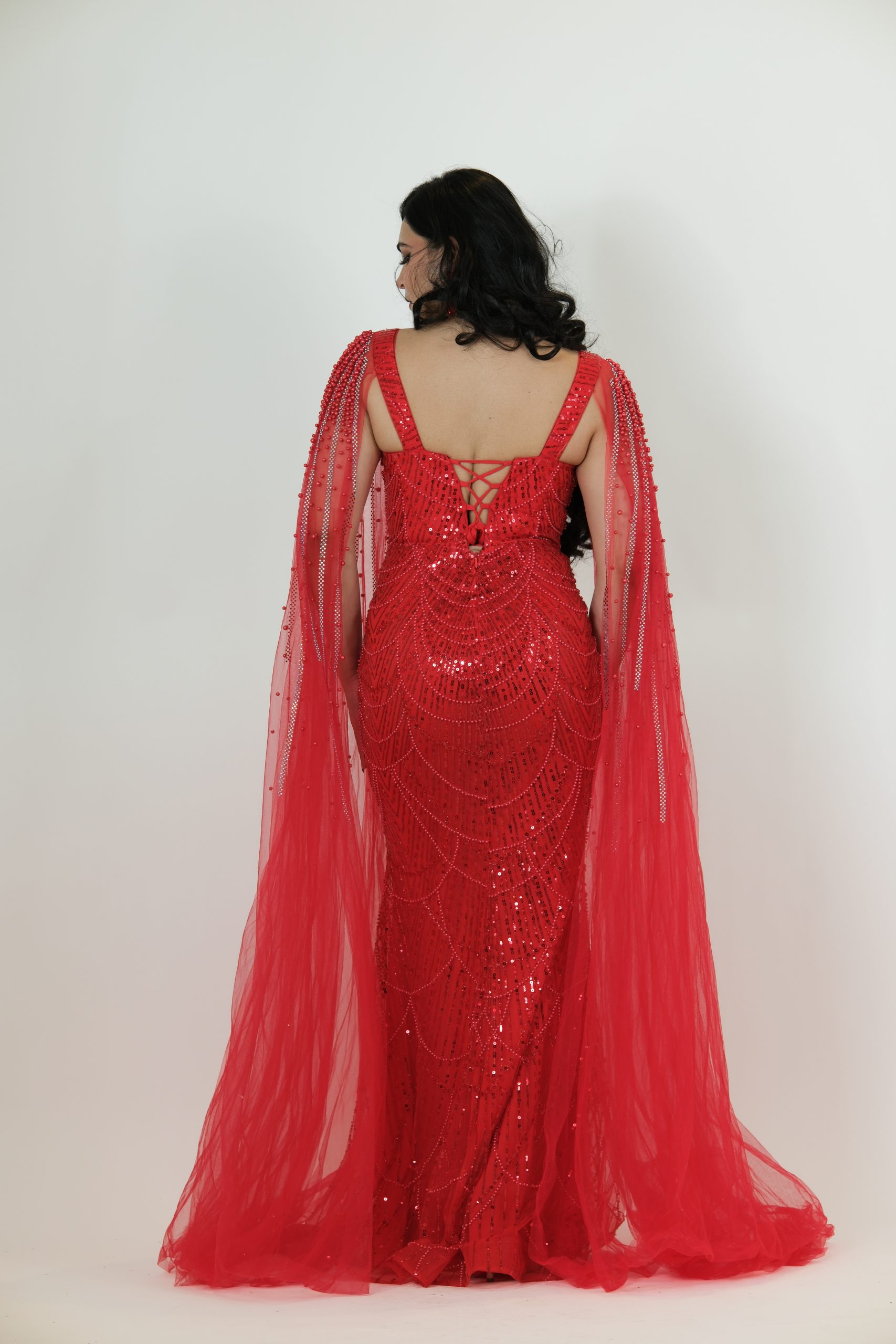 “Red fully beaded gown with scalloped sequin design and dramatic embellished tulle cape.”